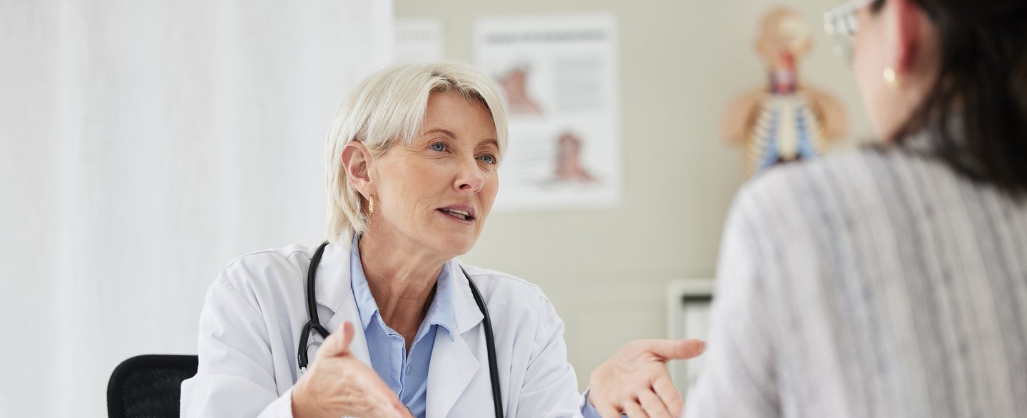 Eine Ärztin sitzt am Tisch und führt ein Gespräch mit einer Patientin.