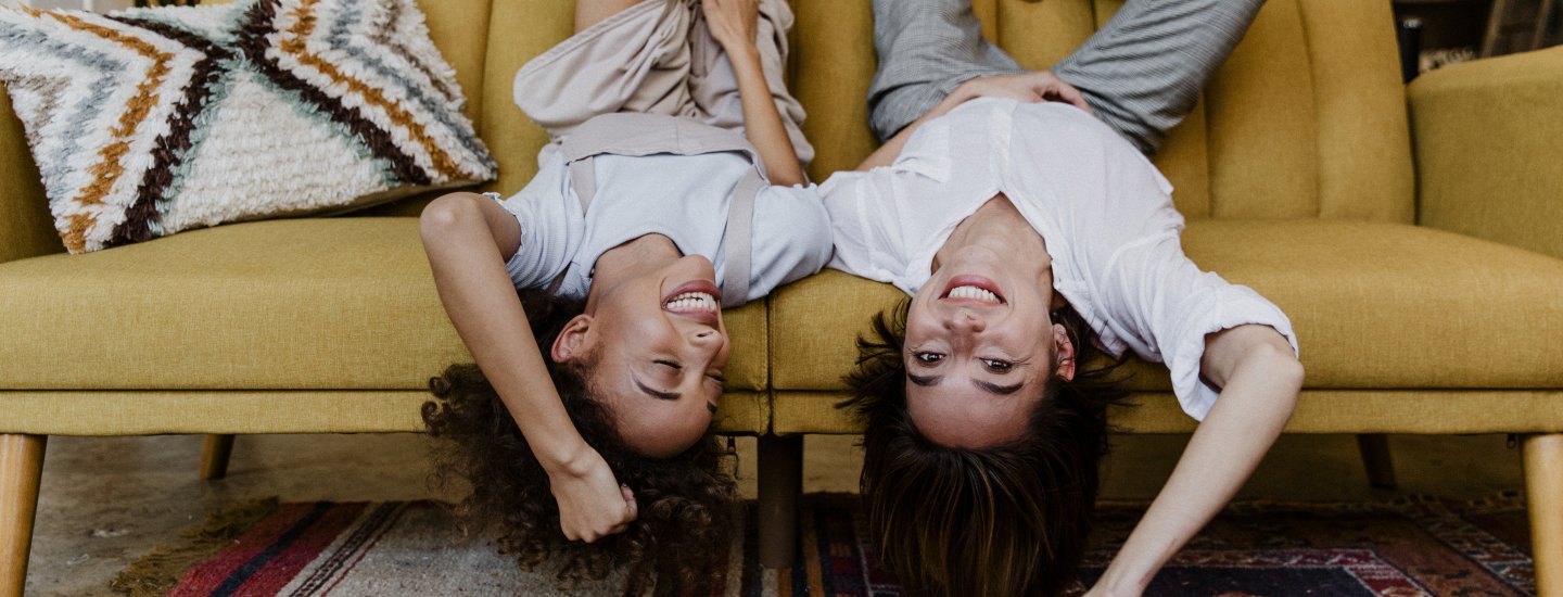 Zwei Frauen liegen kopfüber auf dem Sofa und lachen